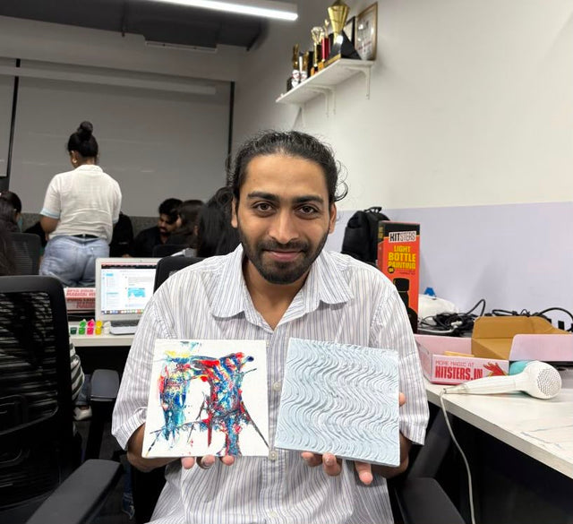 A colleague at his desk holding up two finished paintings, one in each hand