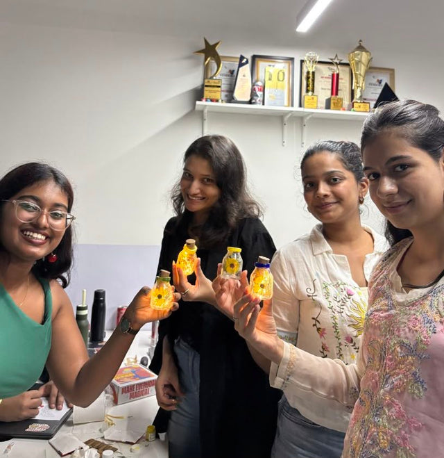 Four colleagues standing together holding up the glass jars they have painted, lit from within