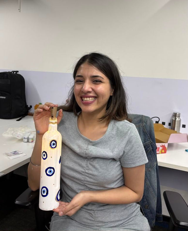 A colleague holding up a tall bottle she has painted with evil-eye motifs