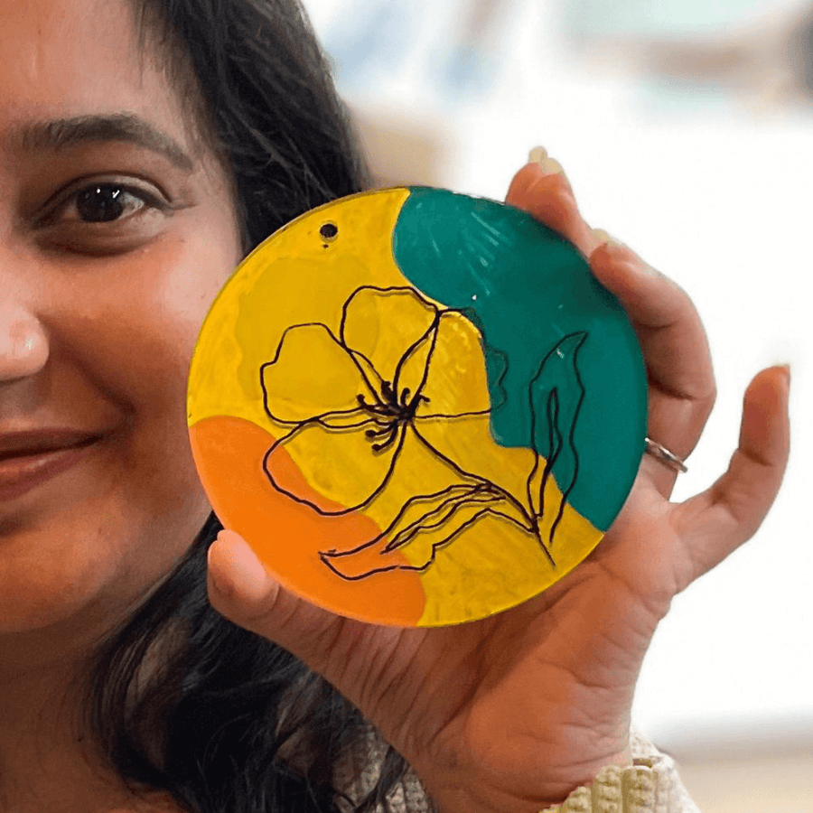 A maker holding up the wooden coaster she has just hand-painted