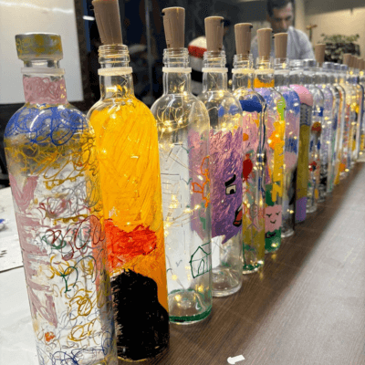 A long row of hand-painted bottle lamps glowing after a Kitsters workshop