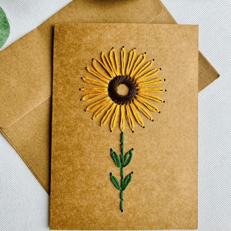 A hand-embroidered sunflower card resting on its plain kraft-paper envelope