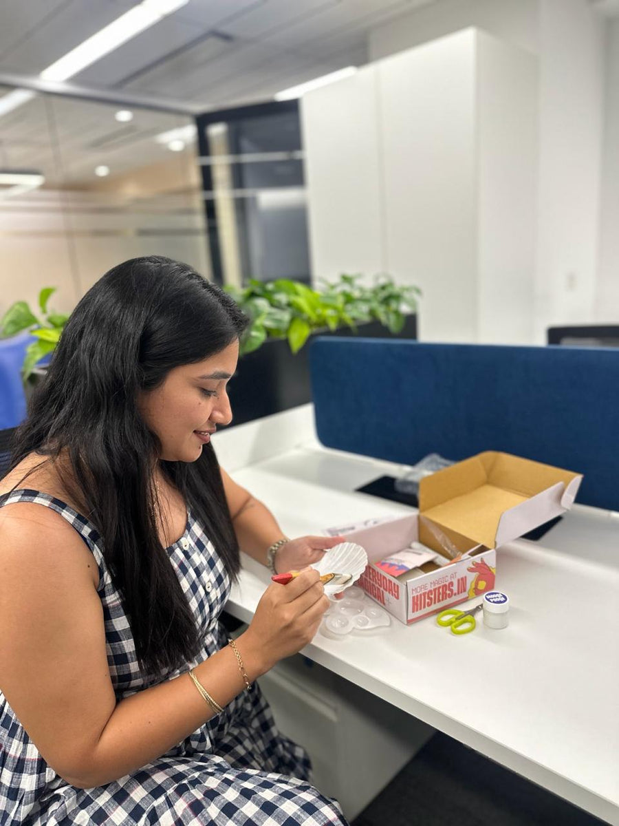 A maker painting a shell at her own desk, her kit box open beside her