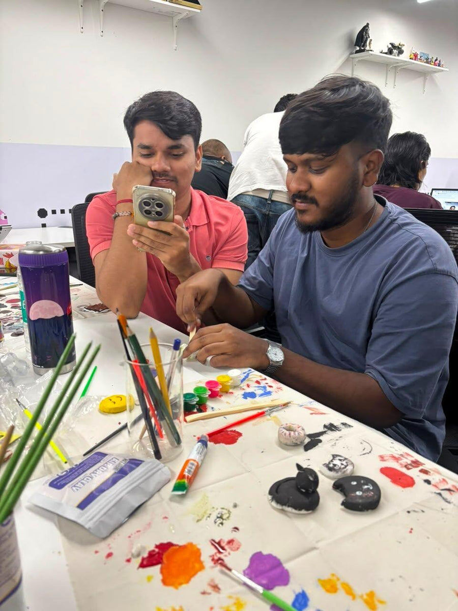 Two colleagues at a paint-covered table, part-way through painting stones