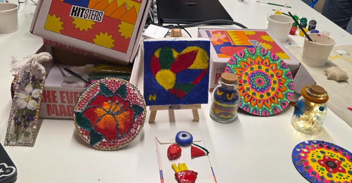 Finished pieces laid out along a table - painted coasters, a sand-art canvas, glow jars and magnets